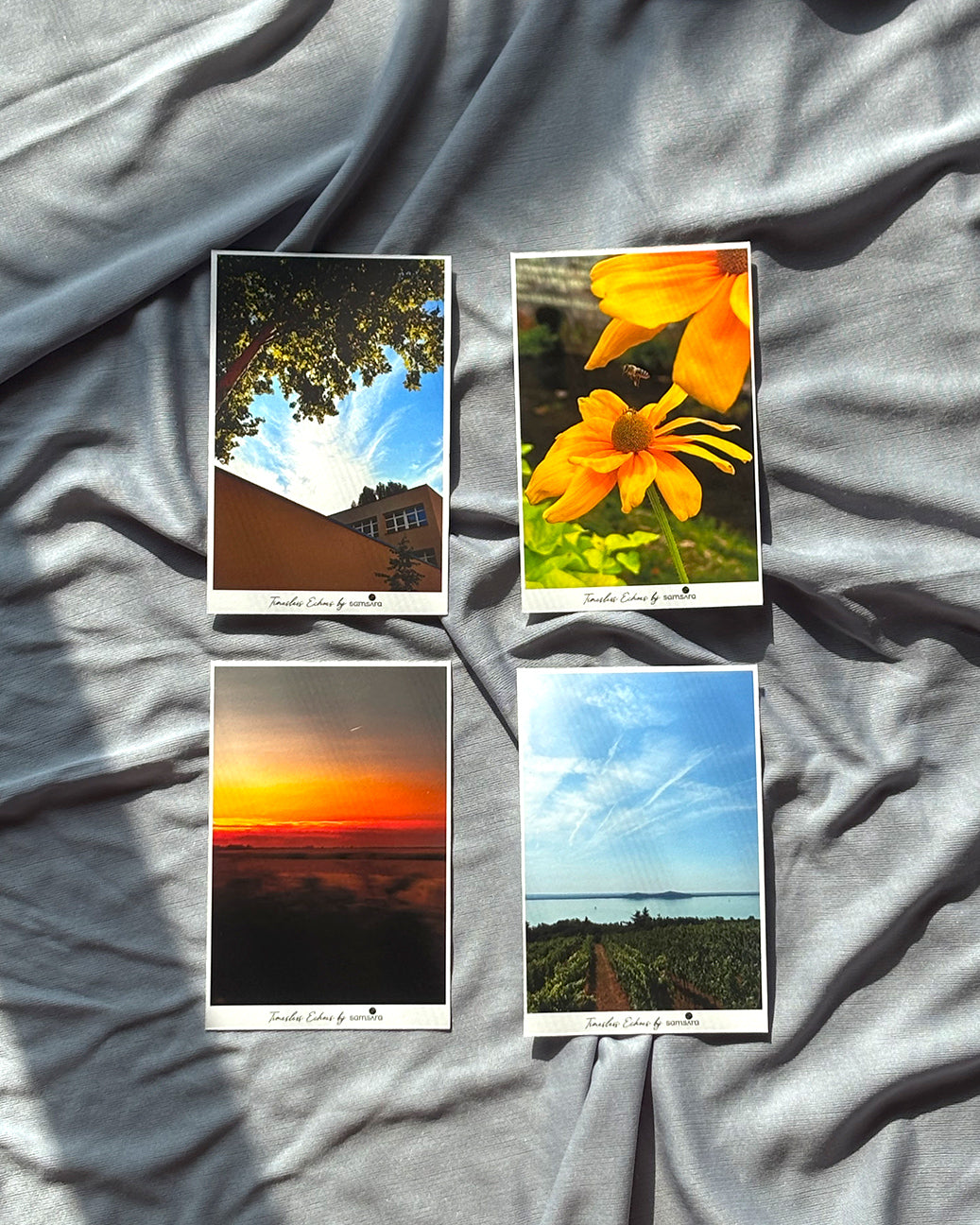 A set of four mini nature art prints displayed on a grey surface, featuring a variety of natural scenes including a sunset, a sunflower, a view of the sky, and a close-up of leaves.